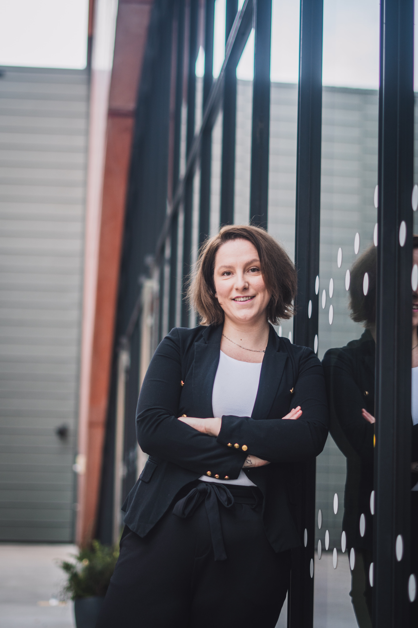 Profesionální business portrét usměvavé ženy v saku, opírající se o moderní prosklenou budovu.