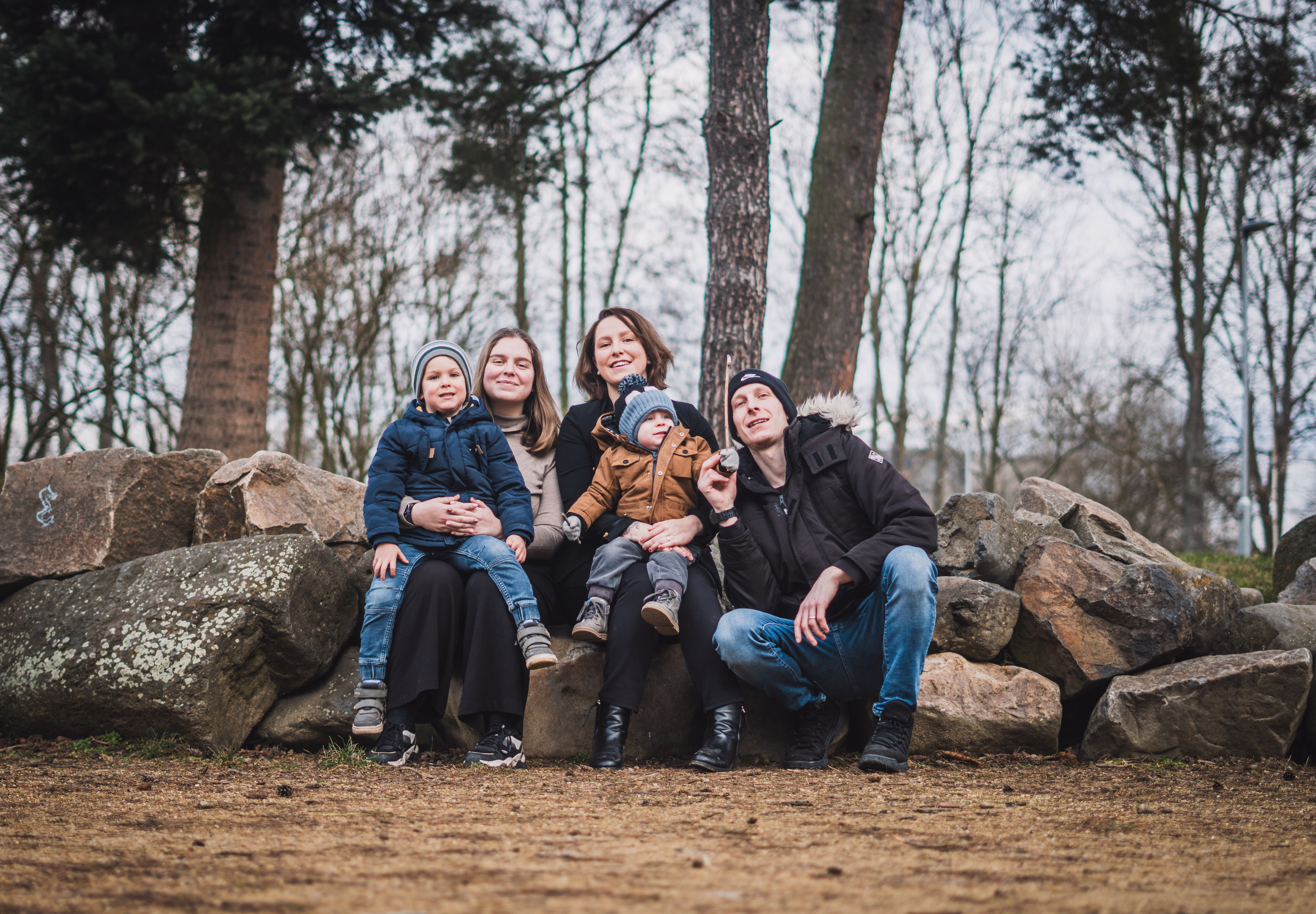 Usměvavý rodinný portrét pětičlenné rodiny s dětmi, sedící na velkých kamenech v parku.